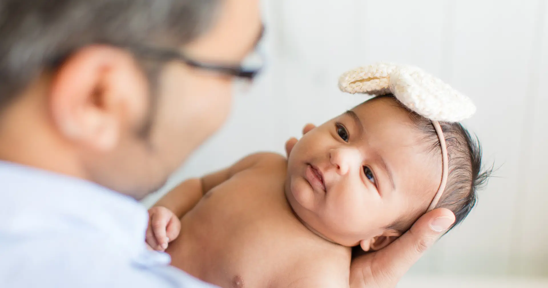 Newborn Care Specialist blurred in foreground holding baby with bow on its head.