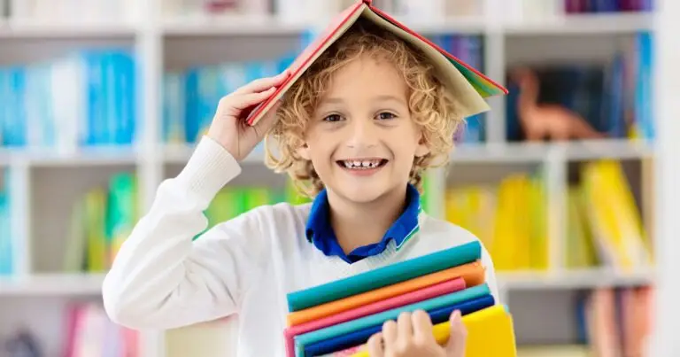 School-aged child holding books with a book on his head. He is smiling, and excited to learn from his Private Educator!
