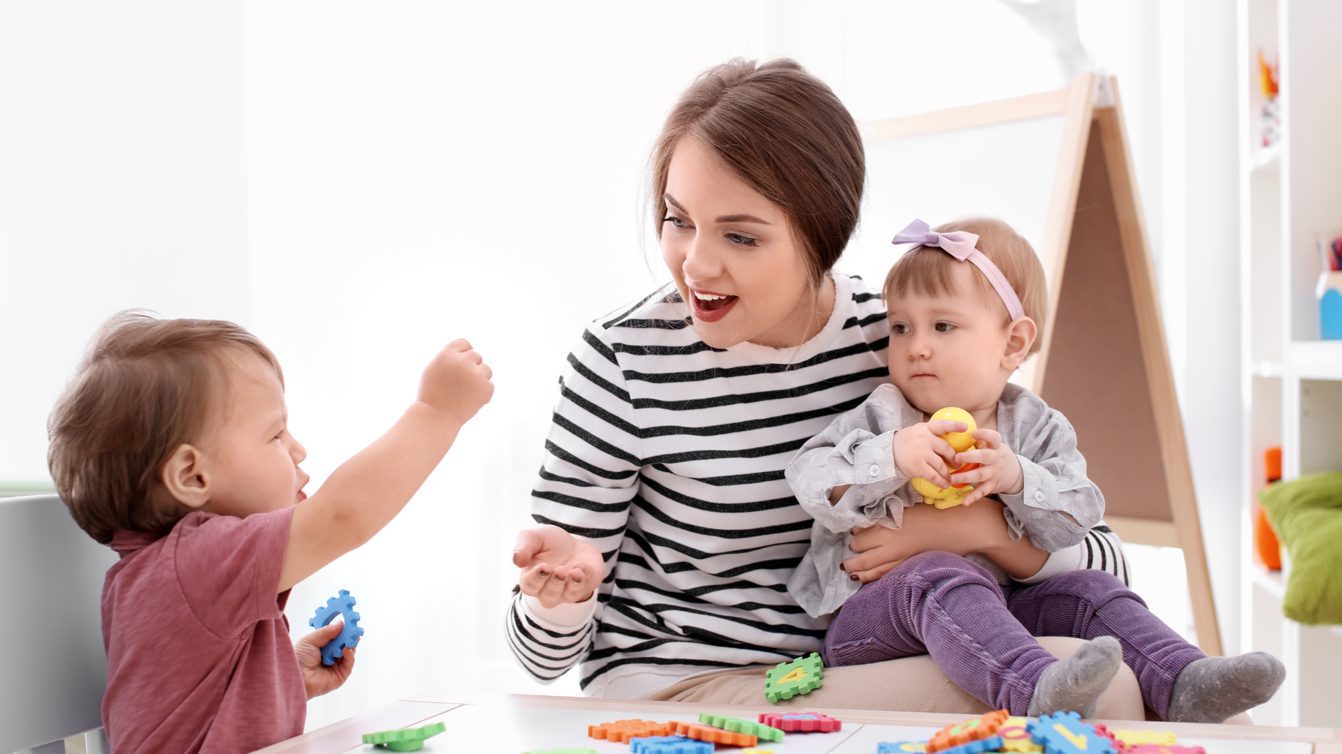 A baby and young child playing with soft foam blocks with their nanny.