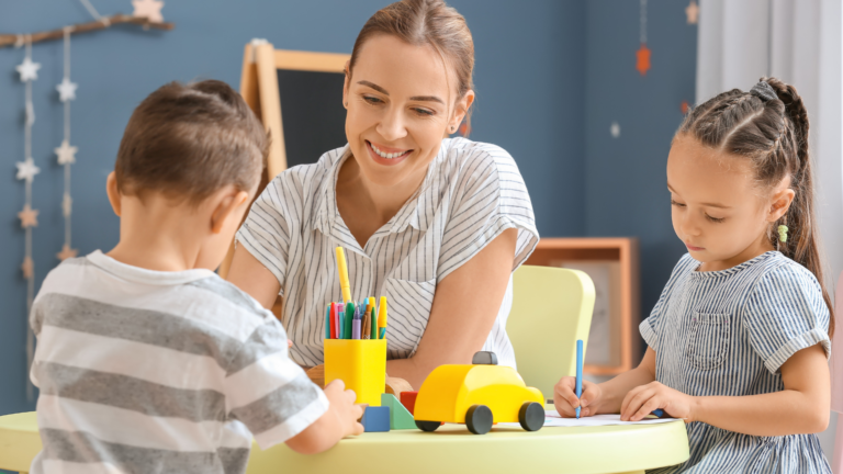 A nanny and two young children playing and drawing in a sunlit playroom